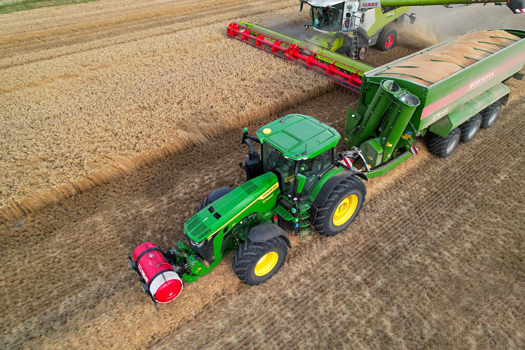 Usługi dronem w rolnictwie. John Deere 8R 410 wiozący przyczepę z zbożem od kombajnu Claas Lexion 8900, zdjęcie wykonane dronem. Kombinat Rolny Kietrz.