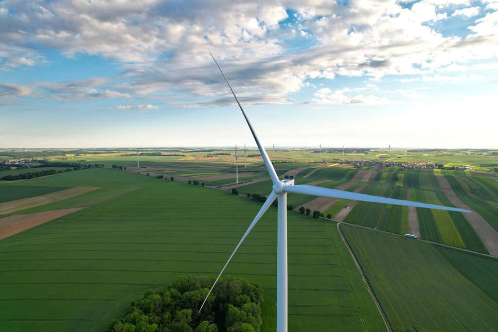 Turbina wiatrowa na tle pól zbożowych uchwycona dronem. Inspekcja dronem. Reklama dronem branży OZE